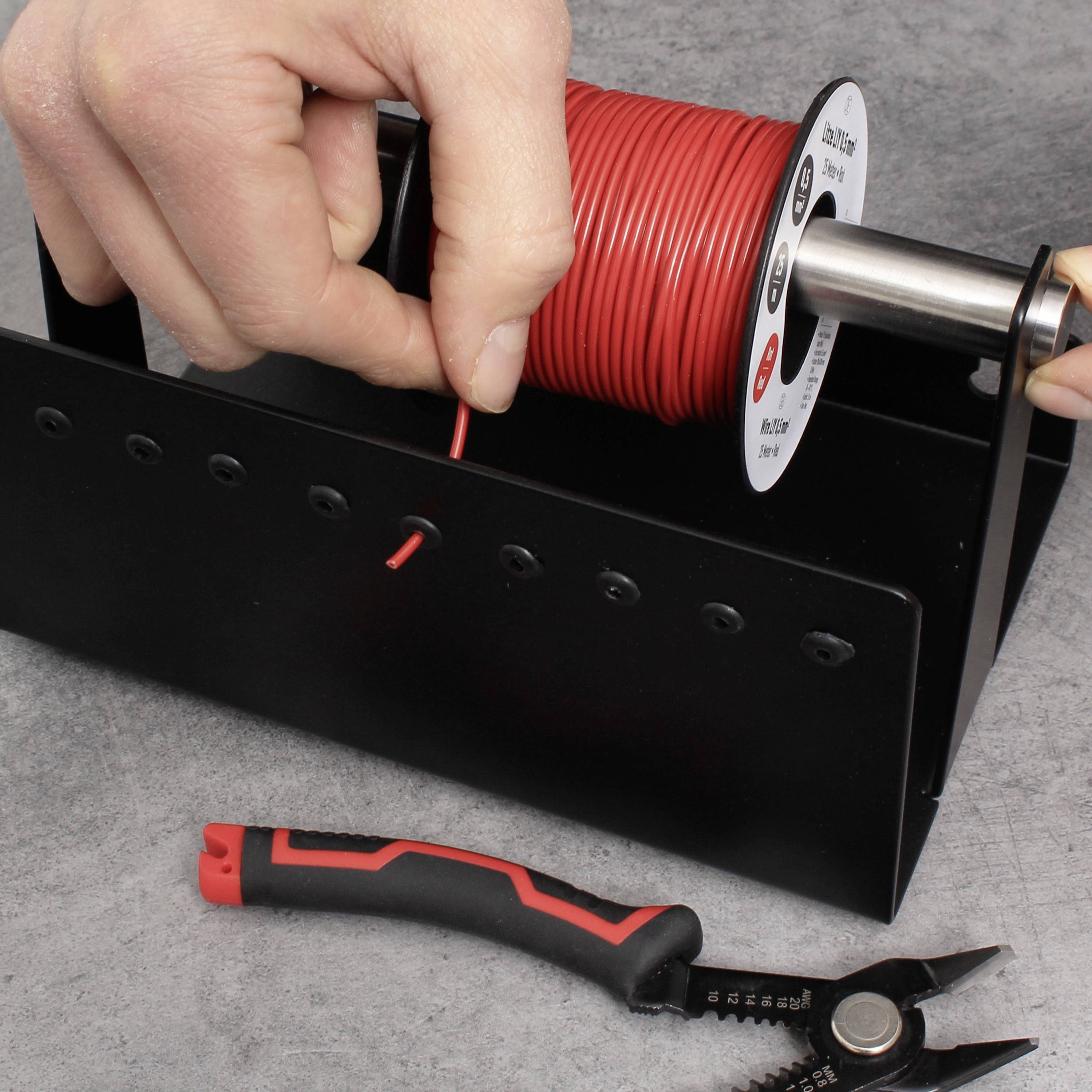 Hand houdt een rode kabelrol vast die is gemonteerd op een standaard; ernaast een kabelsnijder met een rode handgreep op een grijze ondergrond.