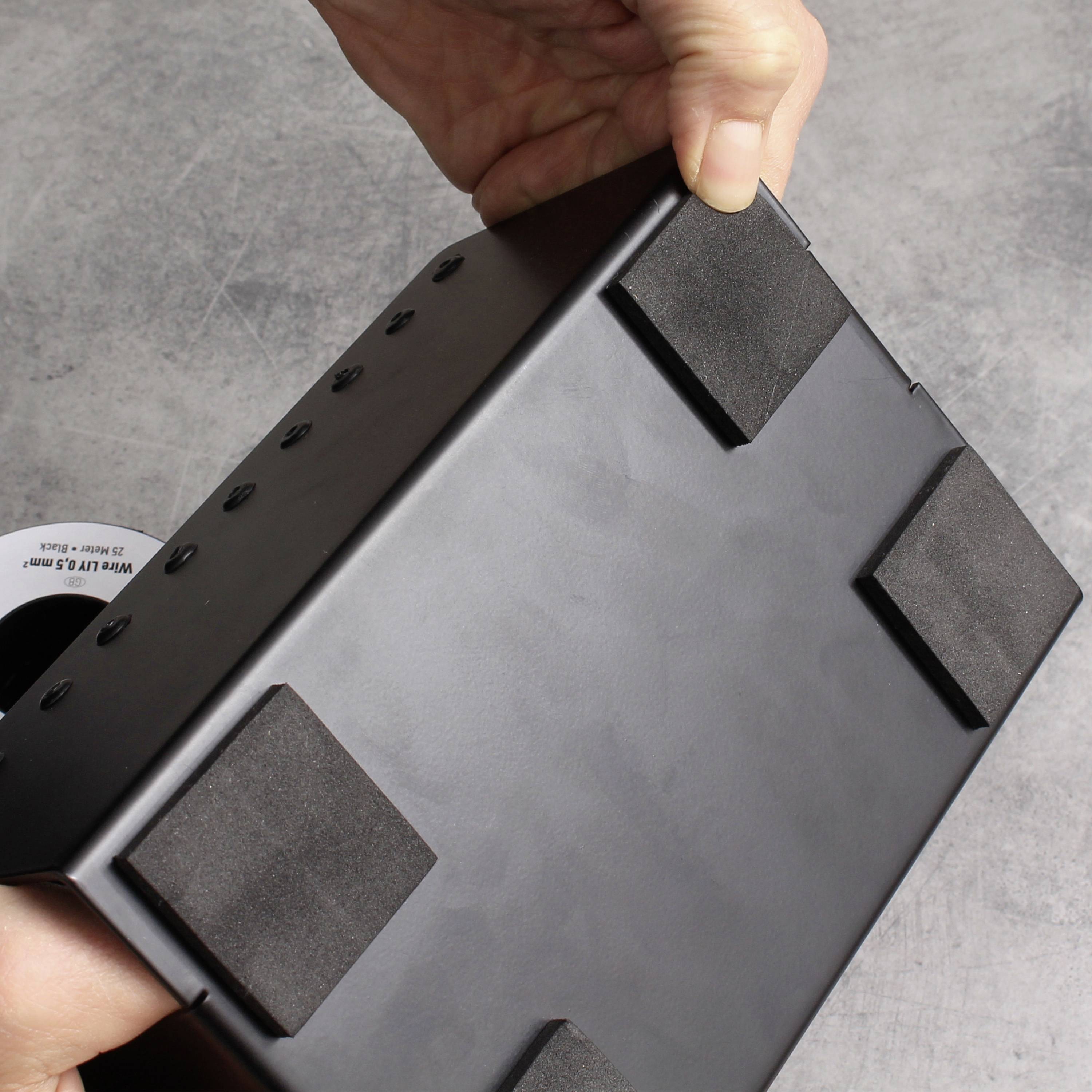 Een hand houdt een zwarte elektronische weegschaal van onderen vast. Vier antislip kussentjes zijn zichtbaar aan de onderkant van de weegschaal.