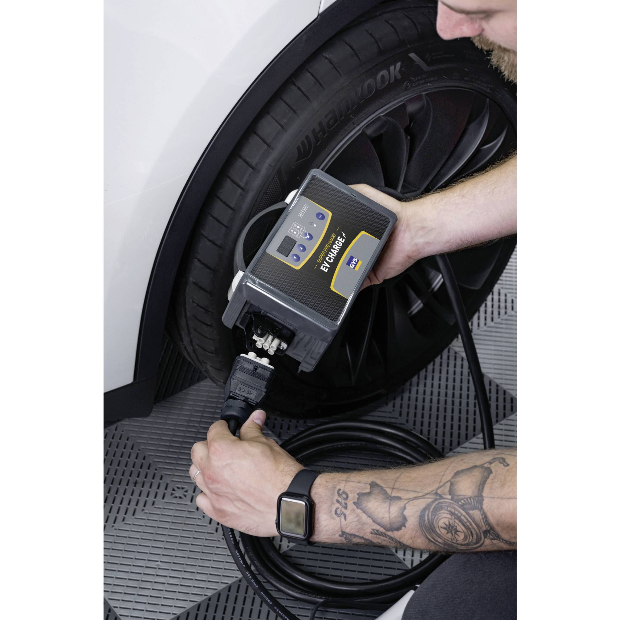 Iemand pompt de band van een auto op met een elektrische luchtpomp. Het apparaat toont de drukmeter. Voertuig staat in een garage op een grijze vloer.