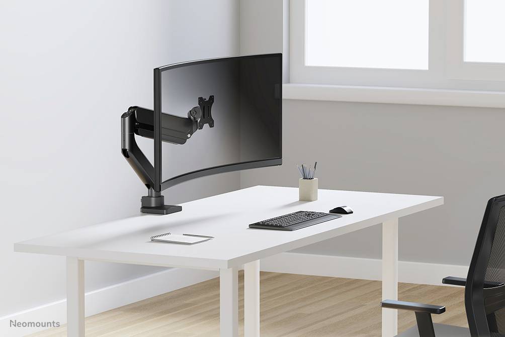 Een leeg bureau met een gebogen monitorsteun, toetsenbord en muis; raam op de achtergrond.