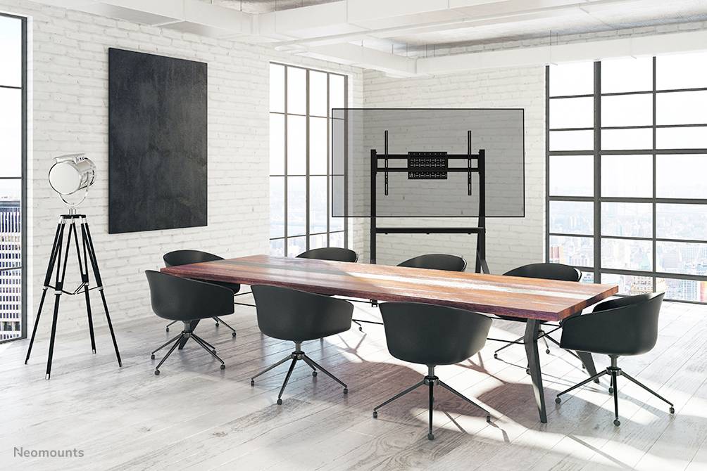 Vergaderzaal met een lange houten tafel, omgeven door zeven zwarte stoelen. Op de achtergrond staat een grote monitor op een standaard.