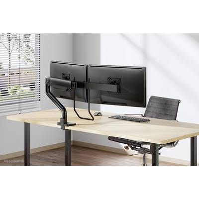 Een bureau met twee schermen gemonteerd op een monitorarm, een toetsenbord en een muis. Naast het bureau staat een stoel.