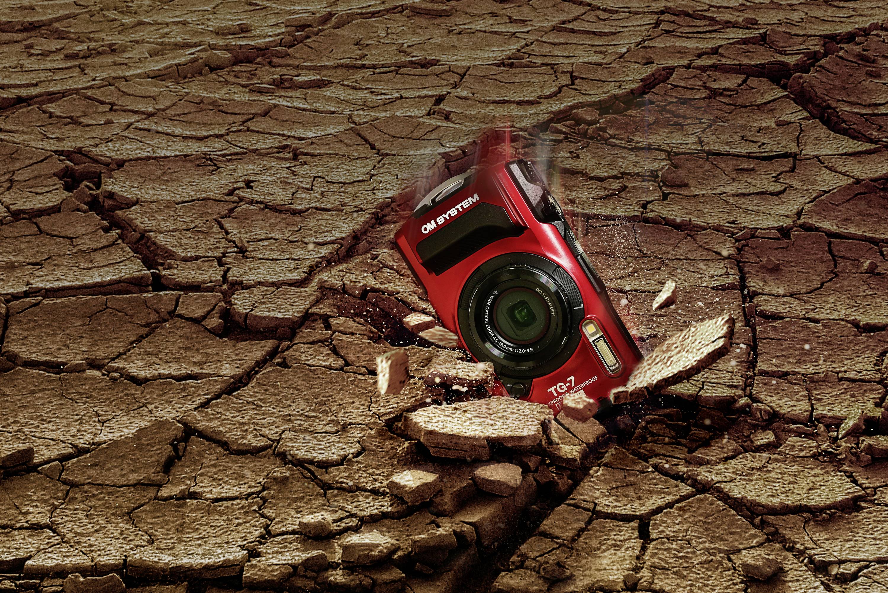 Een rode camera steekt schuin in een droge, gebarsten aardoppervlak. Hij lijkt robuust en veerkrachtig.