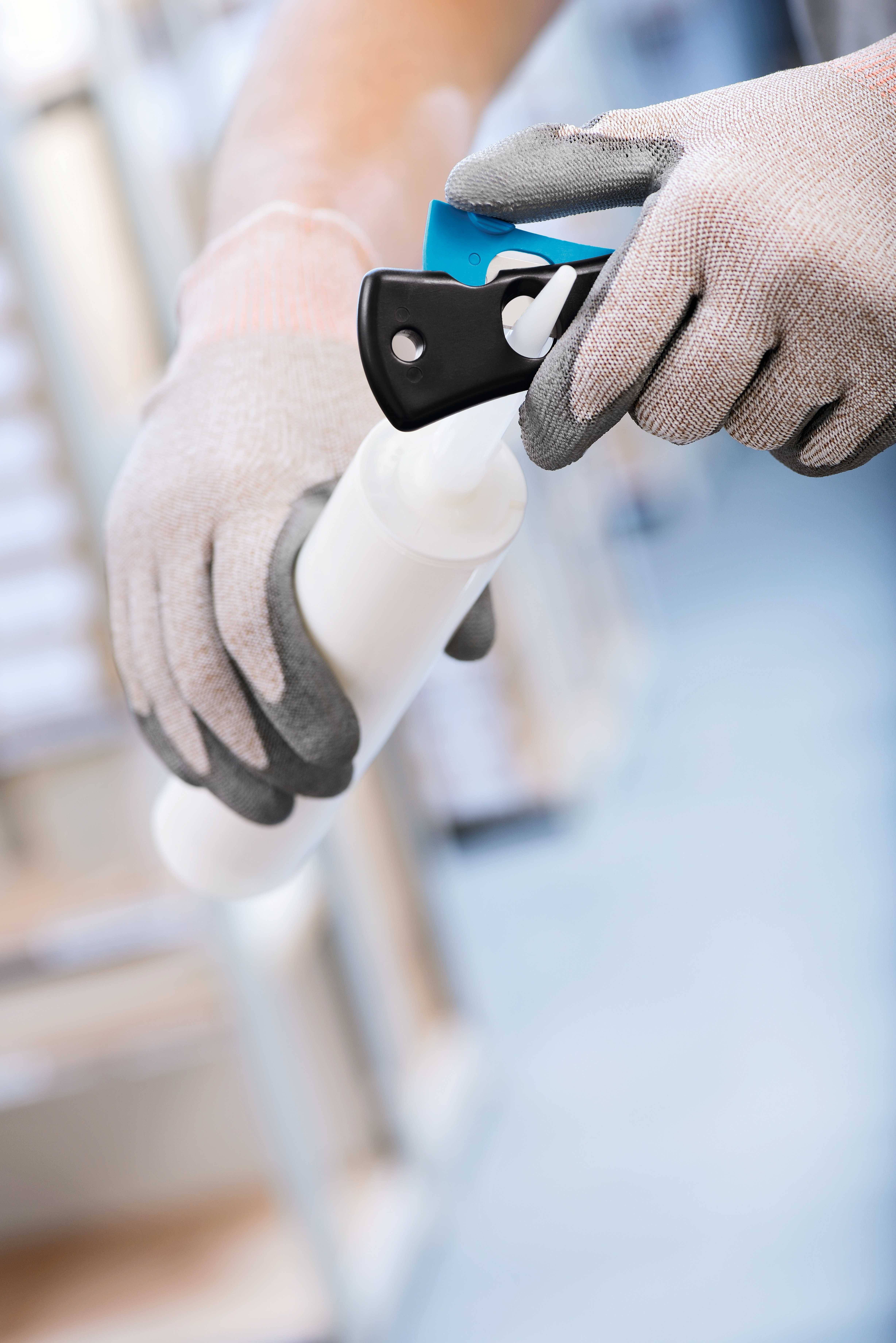 Een persoon met handschoenen houdt een spuitfles vast en verwijdert de beschermkap, waarschijnlijk om te reinigen of te desinfecteren.