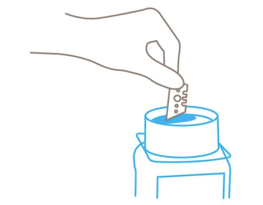 Een hand doopt een scheermesje in een blauwe vloeistof in een container.