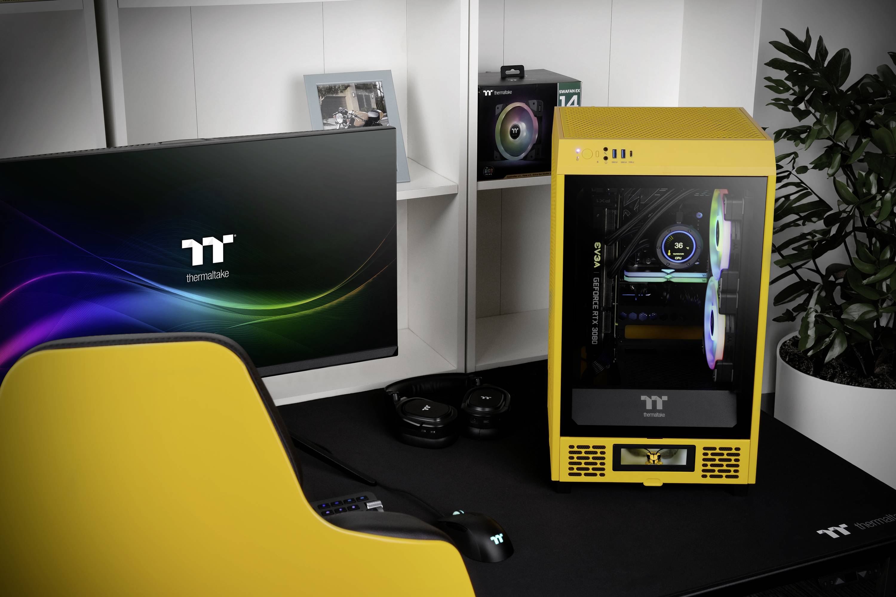 Een geel computerbehuizing met een transparant zijpaneel, op een bureau met een gele bureaustoel, beeldscherm, toetsenbord en koptelefoon.