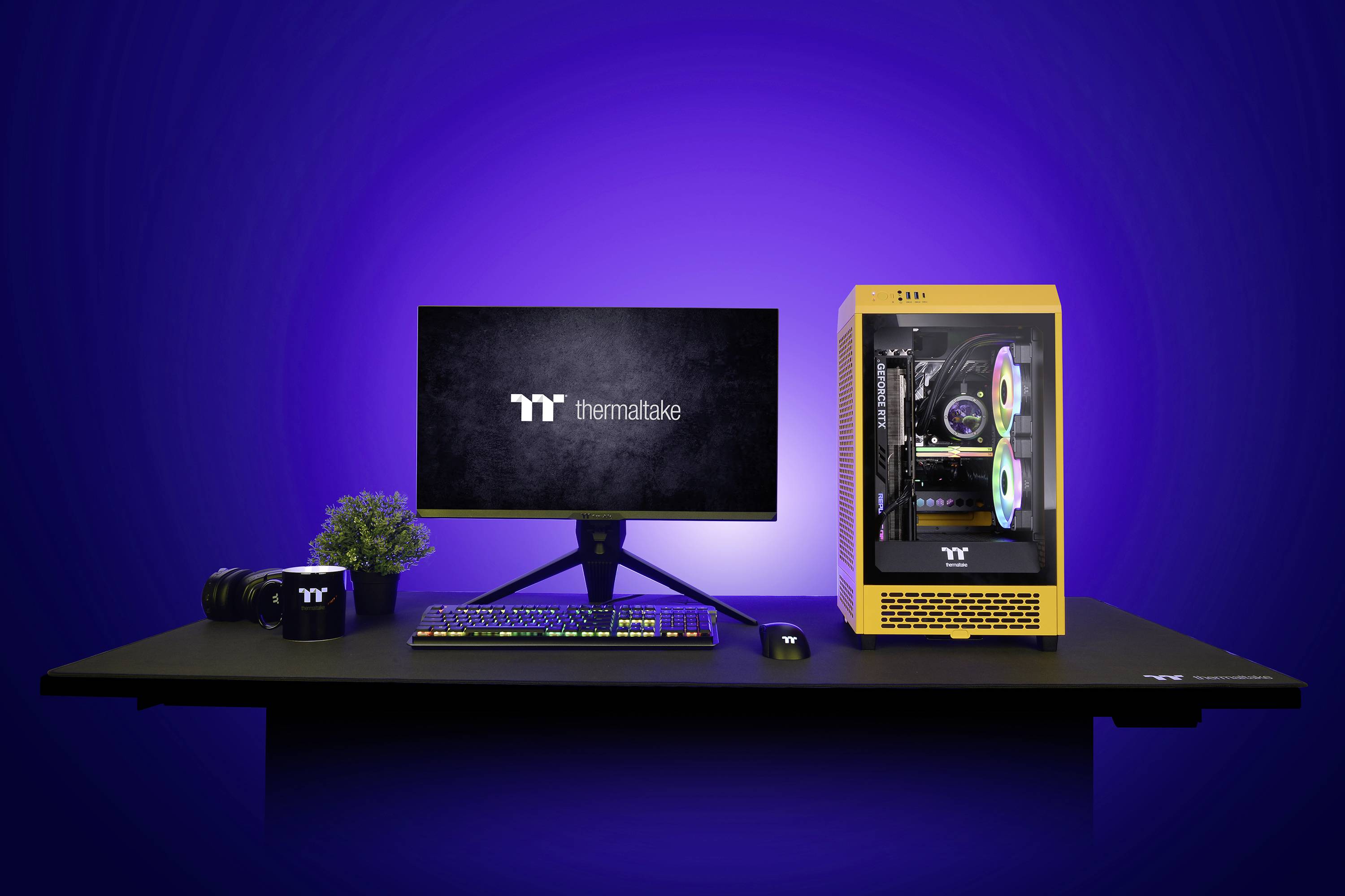 Een gele computer met verlicht interieur staat naast een monitor met het 'Thermaltake'-logo, op een computerbureau met toetsenbord en muis.