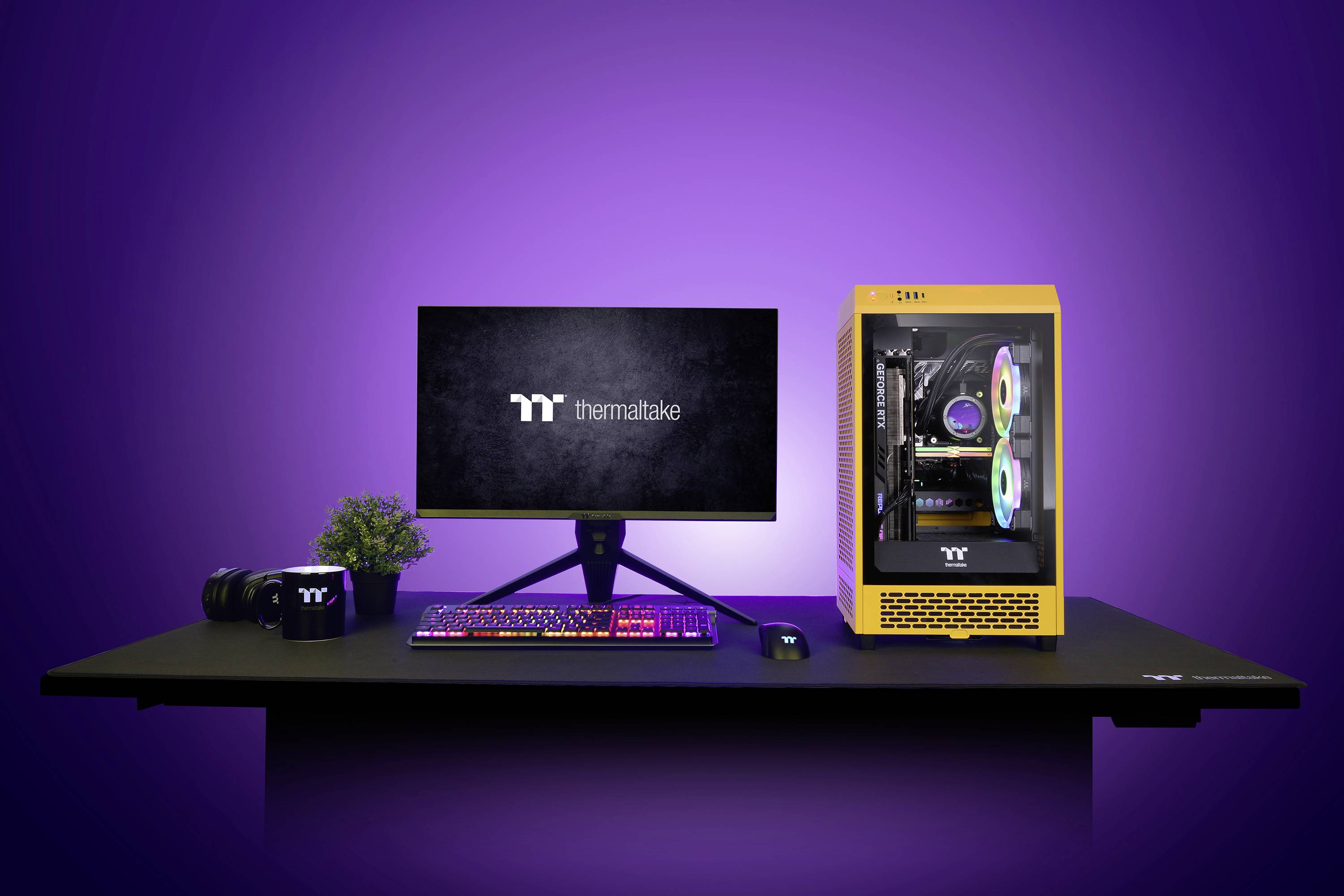 Een bureau met een computer-setup. Monitor toont 'Thermaltake'-logo, met daarnaast toetsenbord, muis, camera, plant en een gele pc-behuizing.