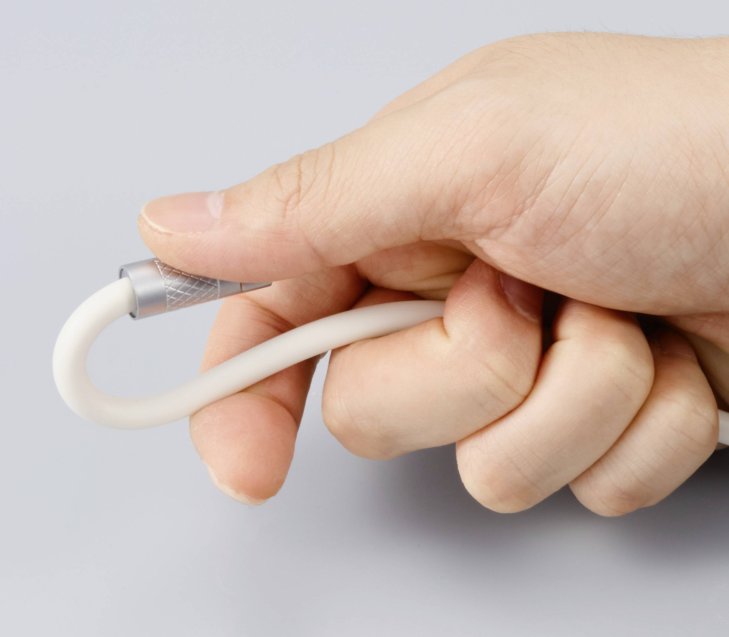 Een hand houdt een gebogen, wit kabel met zilveren aansluiting vast, mogelijk een data- of oplaadkabel, tegen een grijze achtergrond.