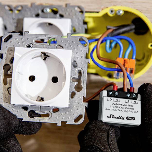 Twee stekkerdoosmodules en een open behuizing met een Shelly PM Mini Gen3. Iemand houdt het module vast en bereidt de installatie voor.