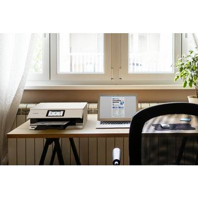 Een bureau met een geopende laptop waarop een document zichtbaar is, naast een printer en een kamerplant. Op de achtergrond een raam.