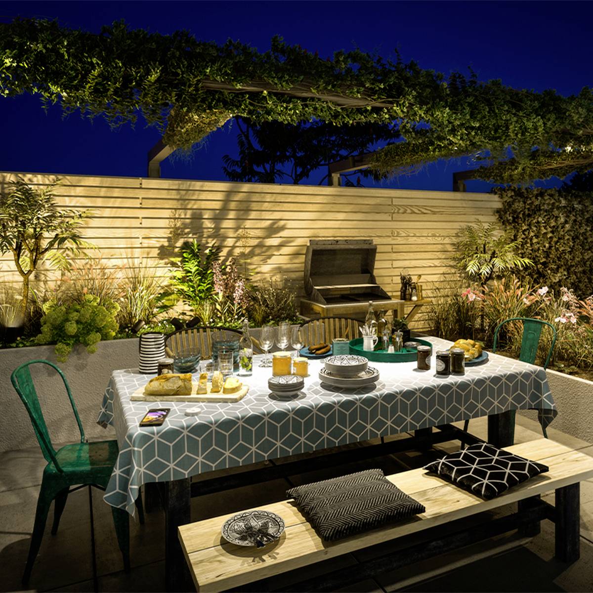 Een feestelijk gedekte tafel op een terras bij nacht. De tafel is versierd met verschillende dranken, servies en hapjes.