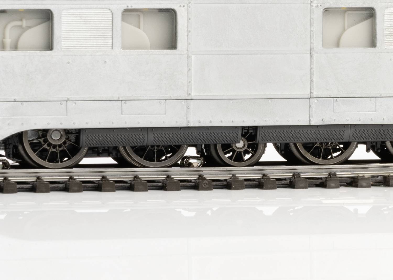 Close-up van een modeltreinwagon met zicht op de wielen en rails. De wagon is grijs en toont fijne details.