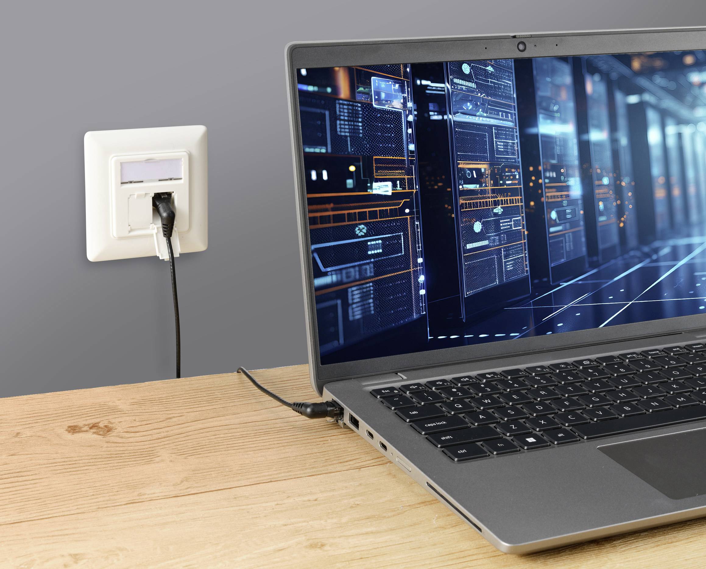 Een laptop op een tafel toont een technische gebruikersinterface, verbonden met een stopcontact aan de muur.