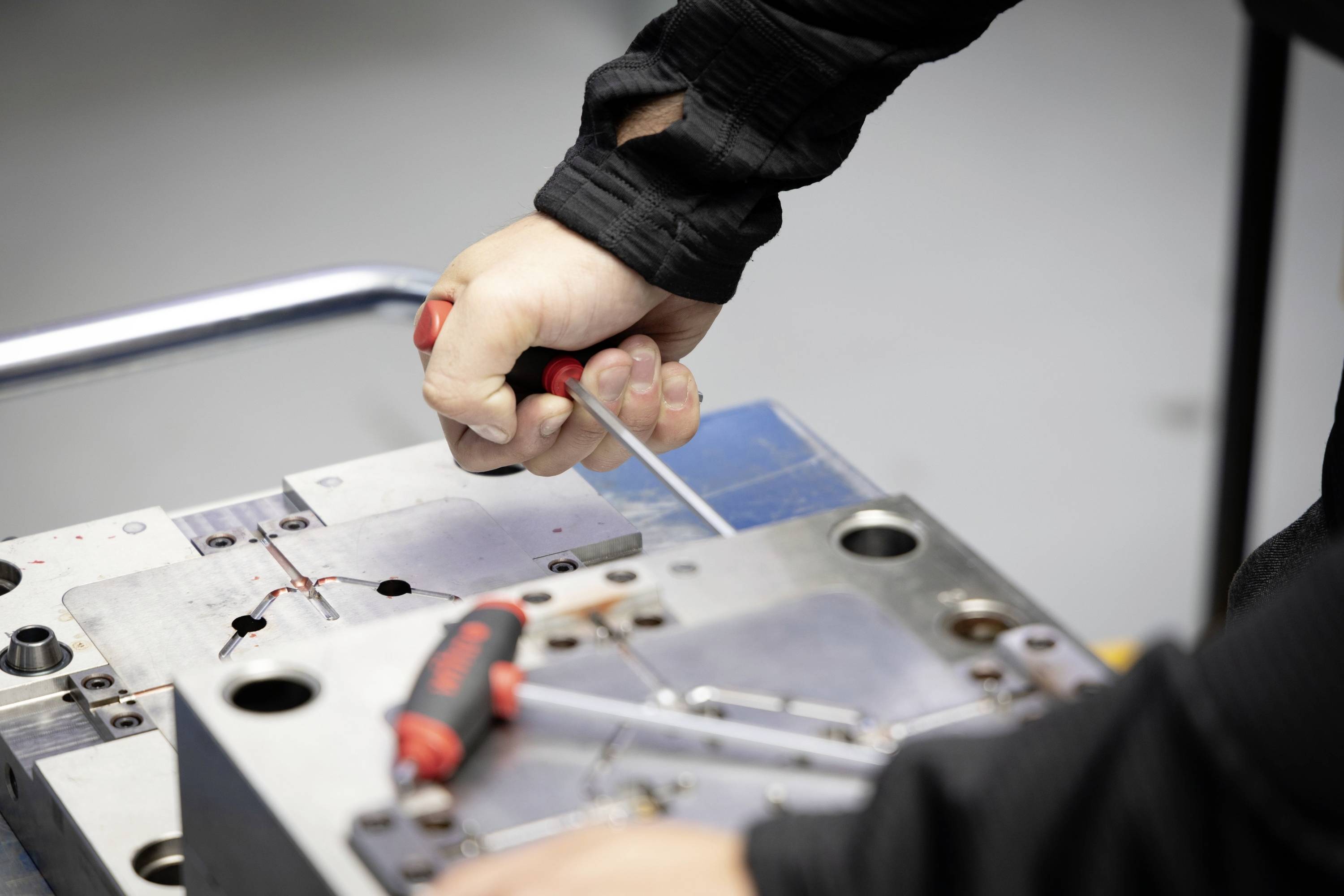 Een persoon stelt een metalen voorziening bij met een schroevendraaier. De focus ligt op precisiewerk en het gebruik van gereedschap.