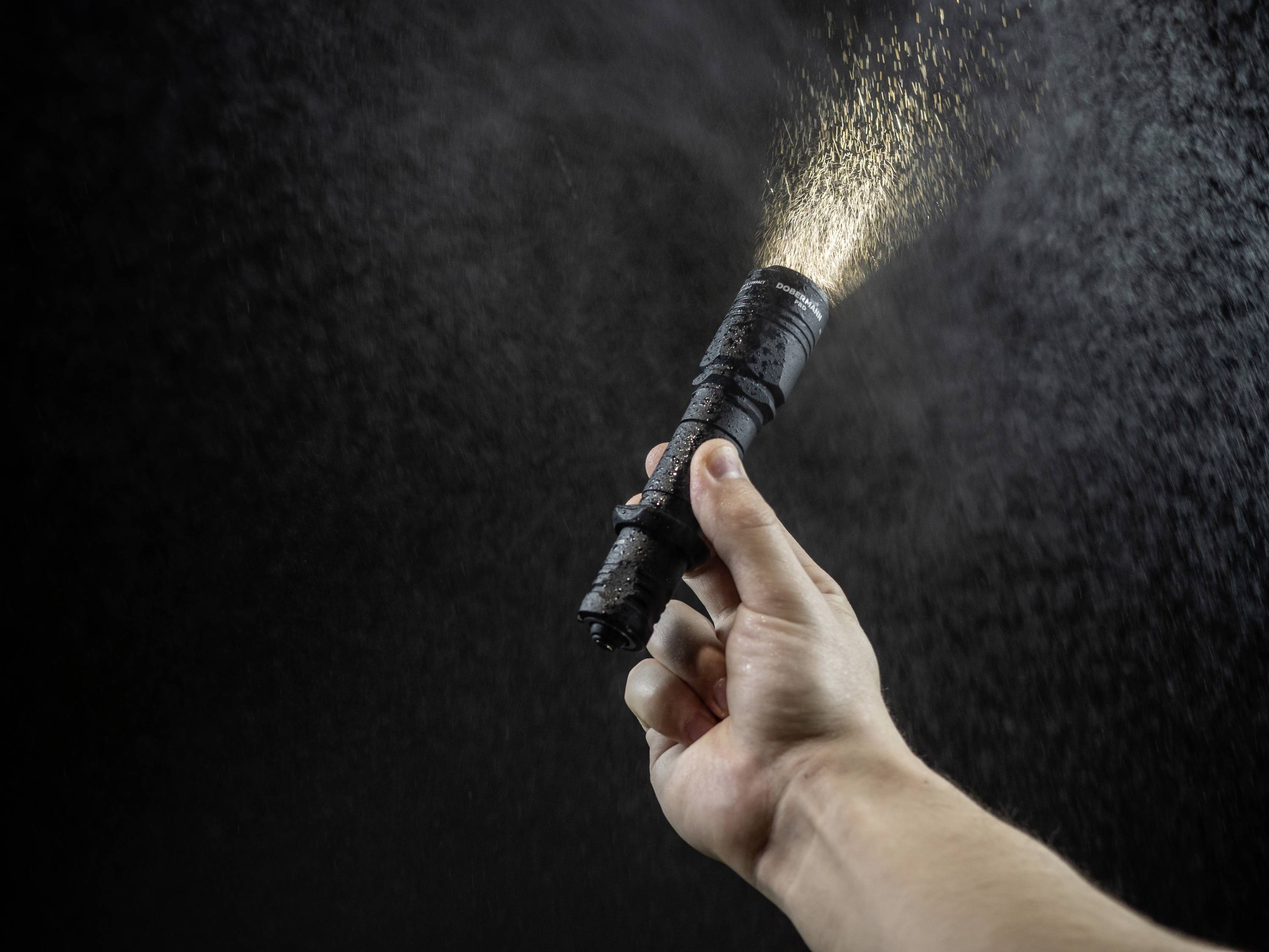 Een hand houdt een zaklamp vast, waaruit een lichtstraal schijnt in de donkere ruimte. Fijn stof of deeltjes zweven in het licht.