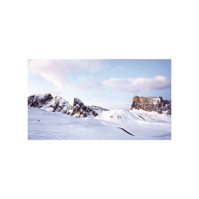 Besneeuwde berglandschap onder een blauwe hemel met enkele wolken. Majestueuze toppen op de achtergrond, een wijds open besneeuwd terrein op de voorgrond.
