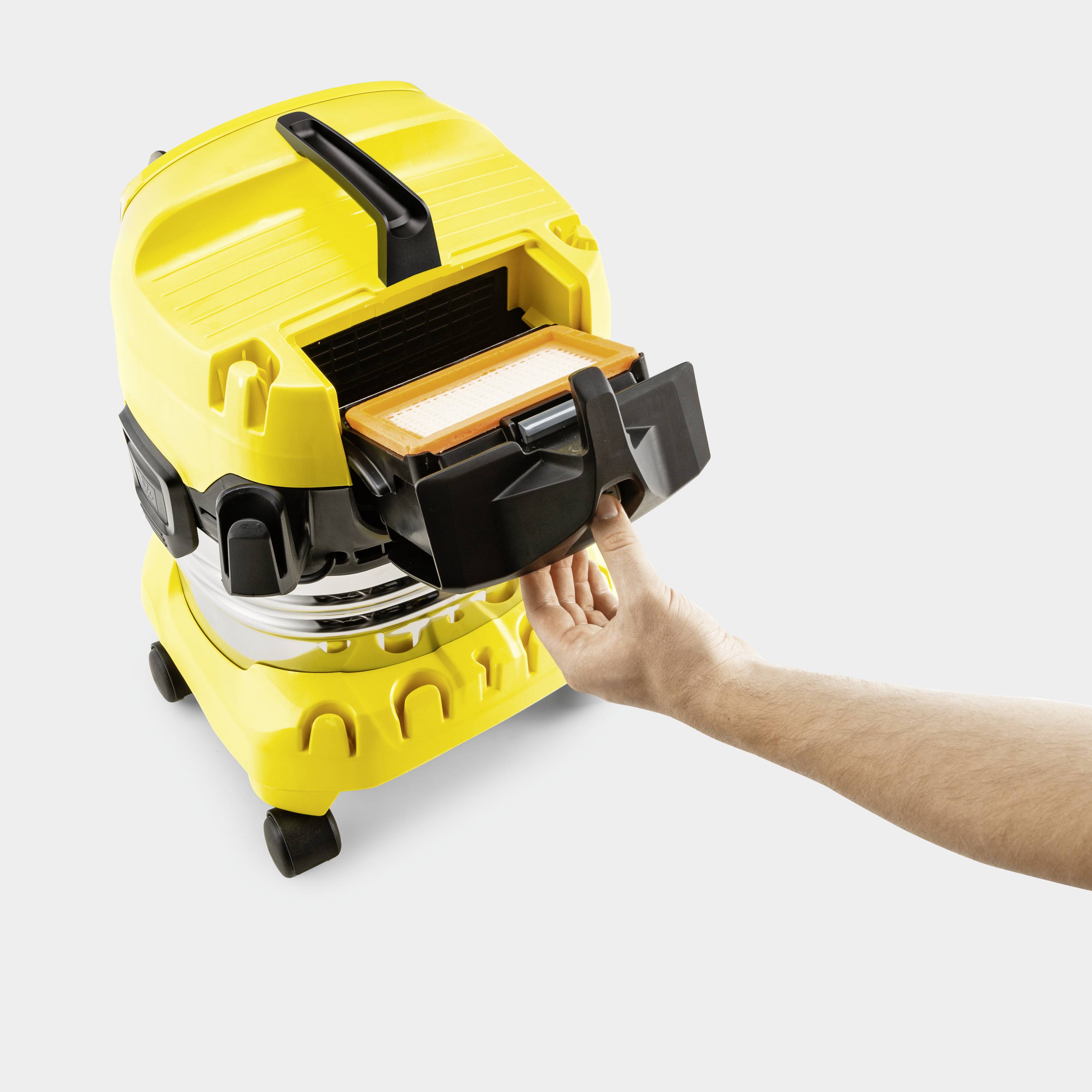 Een gele industriestofzuiger met een open filtervak. Een hand trekt de filter eruit. Dit apparaat wordt gebruikt voor schoonmaakwerkzaamheden.