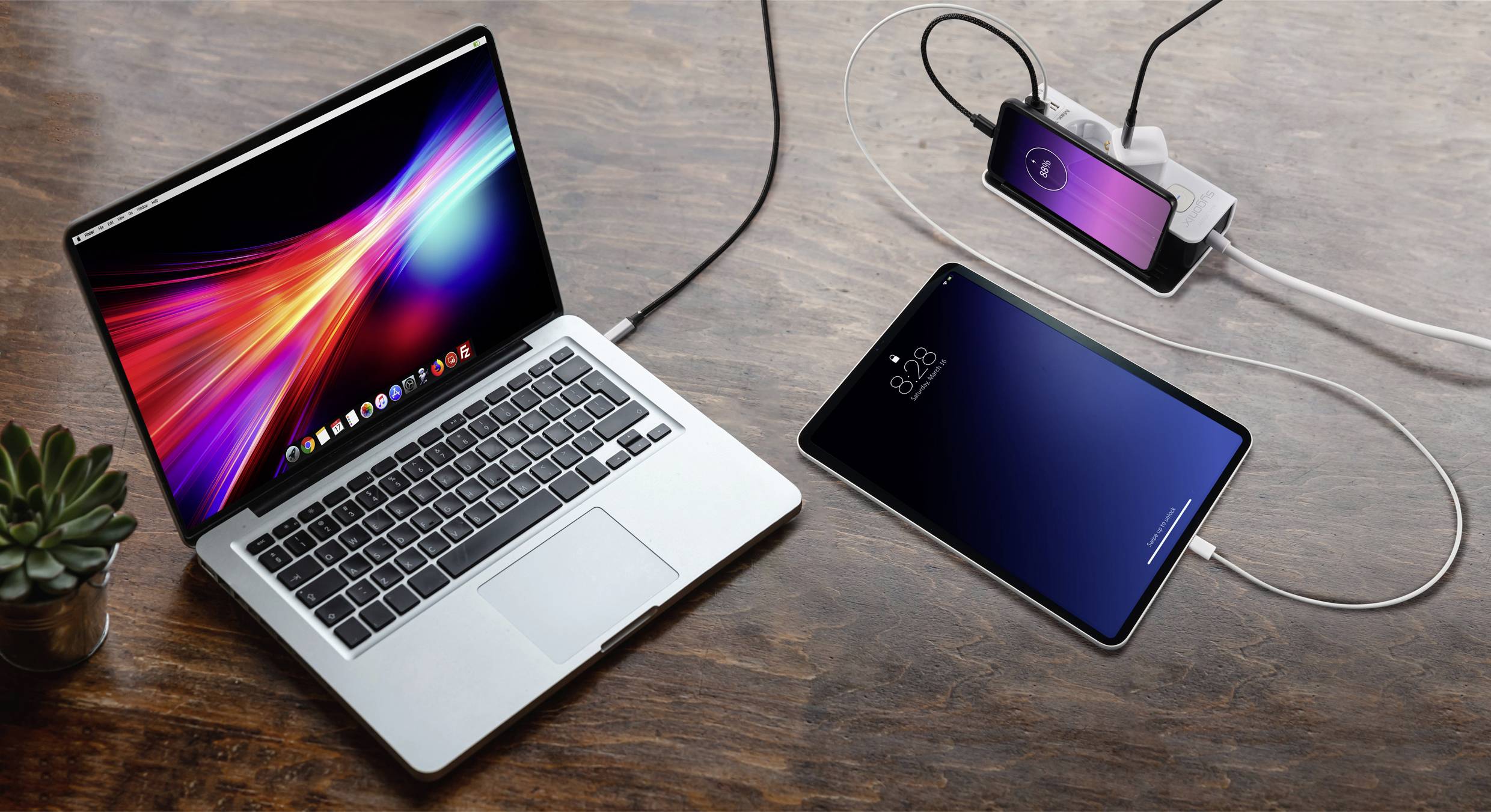 Laptop, smartphone en tablet op houten tafel, alle apparaten worden opgeladen via USB-kabels. Een laptopscherm toont gekleurde golven.