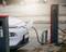 Een witte auto wordt opgeladen bij een elektrische laadpaal op een parkeerplaats. Een kabel verbindt de auto met het laadstation.