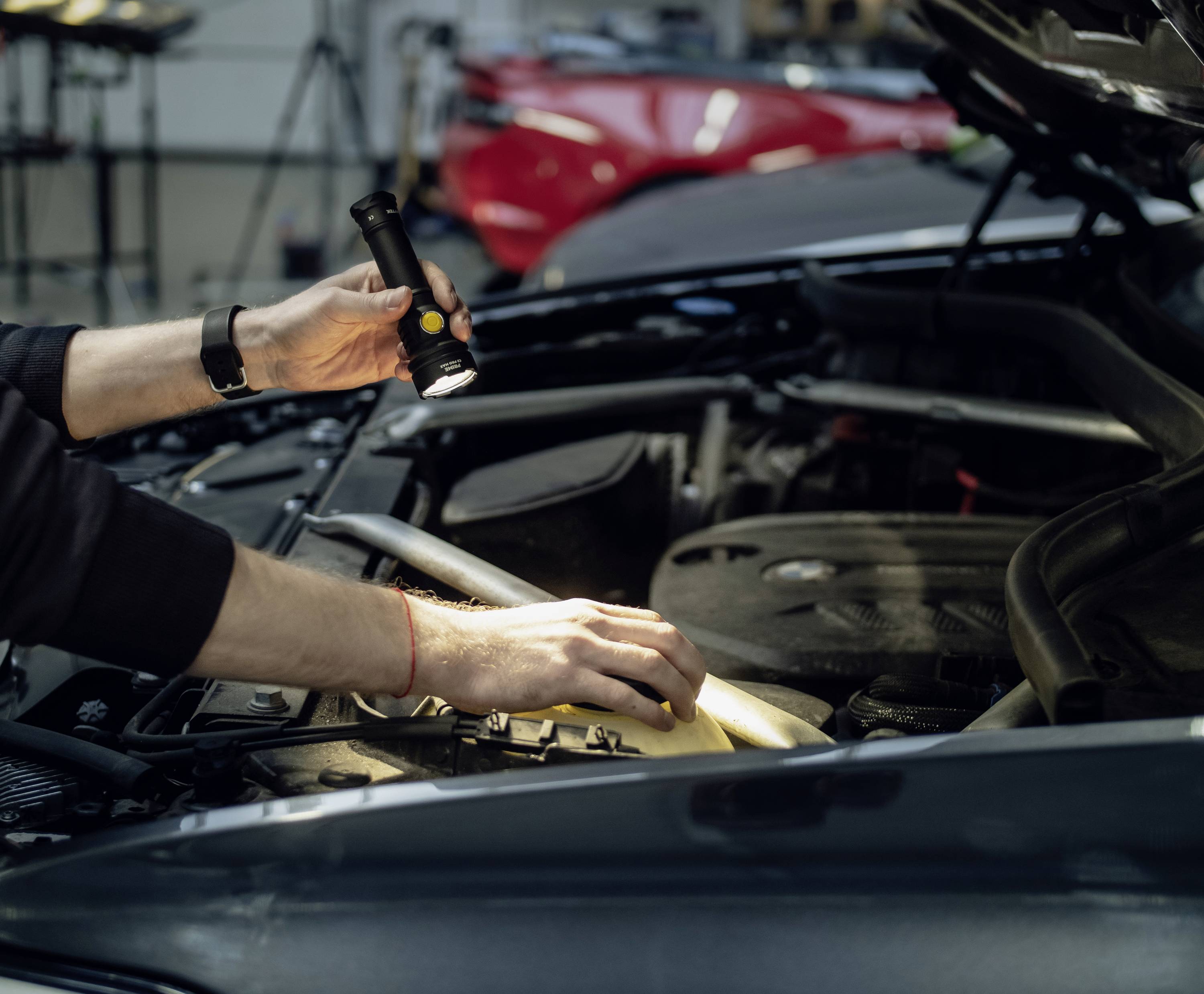Een persoon schijnt met een zaklamp in de motorruimte van een auto, controleert onderdelen en zoekt naar mogelijke problemen.