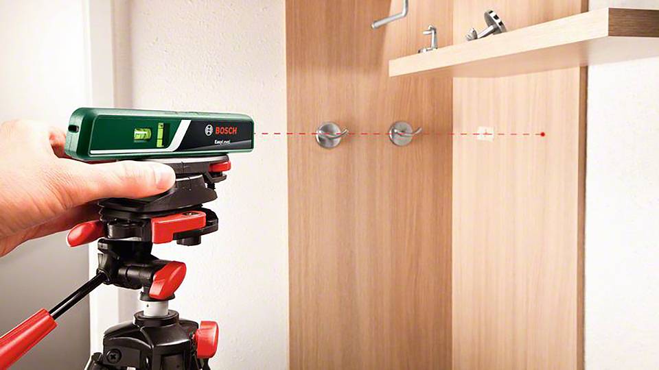 Een vakman gebruikt een lasermetingsapparaat op een statief om nauwkeurig boorgaten in een houten muur te markeren.