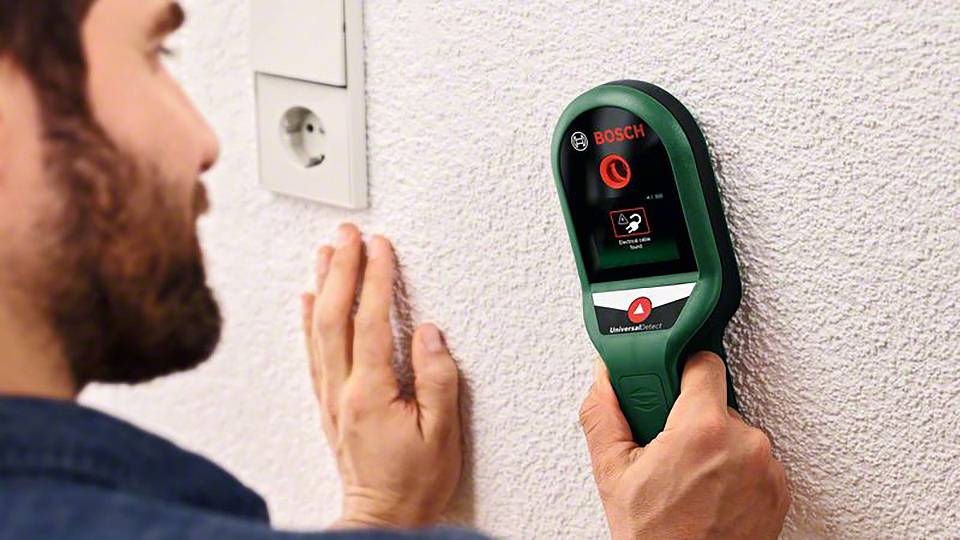 Een man gebruikt een muurscanner van Bosch om leidingen of metaal in de muur te lokaliseren.