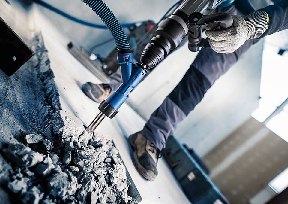 Een bouwvakker gebruikt een pneumatische hamer om beton te breken. Draagt werkhandschoenen en veiligheidsschoenen.