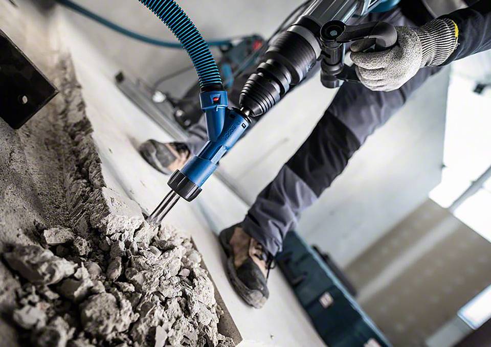 Een persoon bewerkt een betonvloer met een zware breekhamer om deze te verwijderen. Stof en puin zijn zichtbaar.