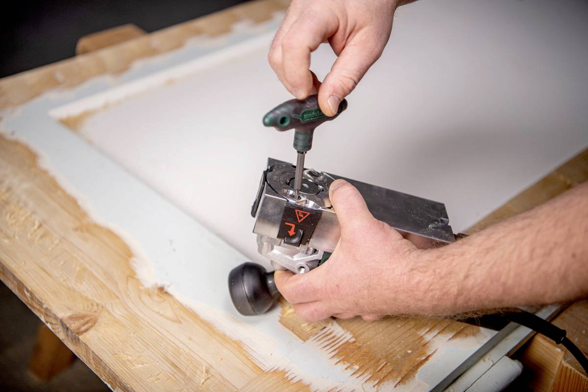 Een persoon werkt met een houtbewerkingsgereedschap om een frame op een houten tafel te bewerken.