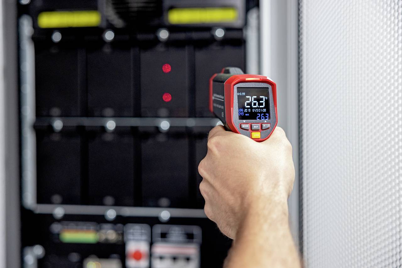 Een handapparaat meet een temperatuur van 26,3 graden Celsius voor een serverrek.