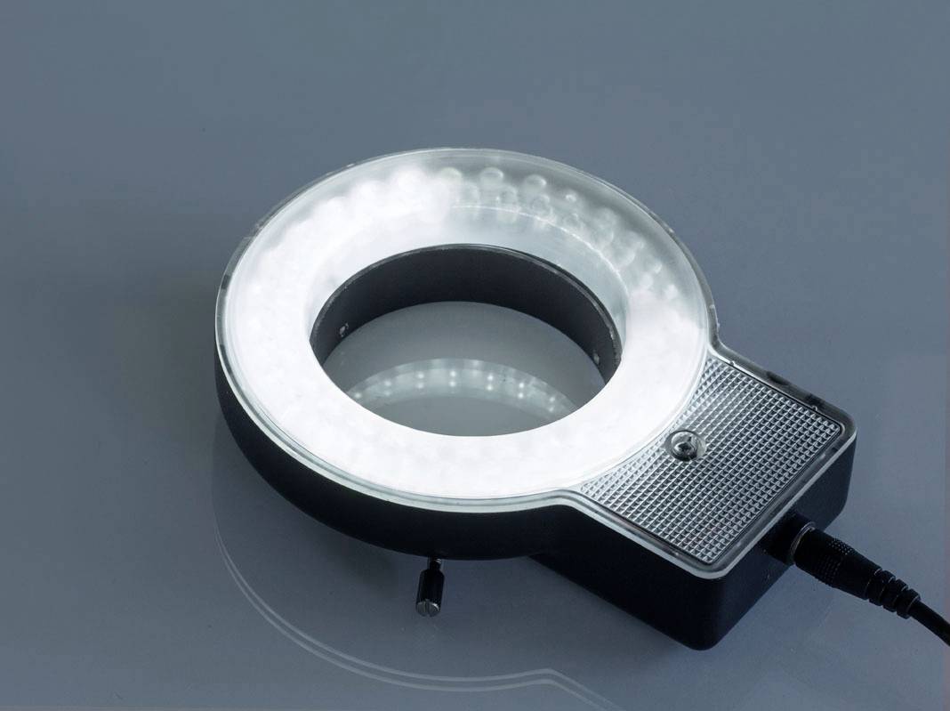 Een rond LED-ringlicht, aangesloten op een kabel, ligt op een gladde, blauwe ondergrond. Het schijnt helder wit.