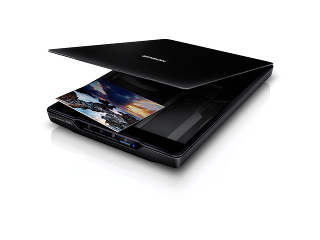 Een flatbedscanner scant een foto met een zonsondergang aan zee. De scanner is zwart en licht geopend.