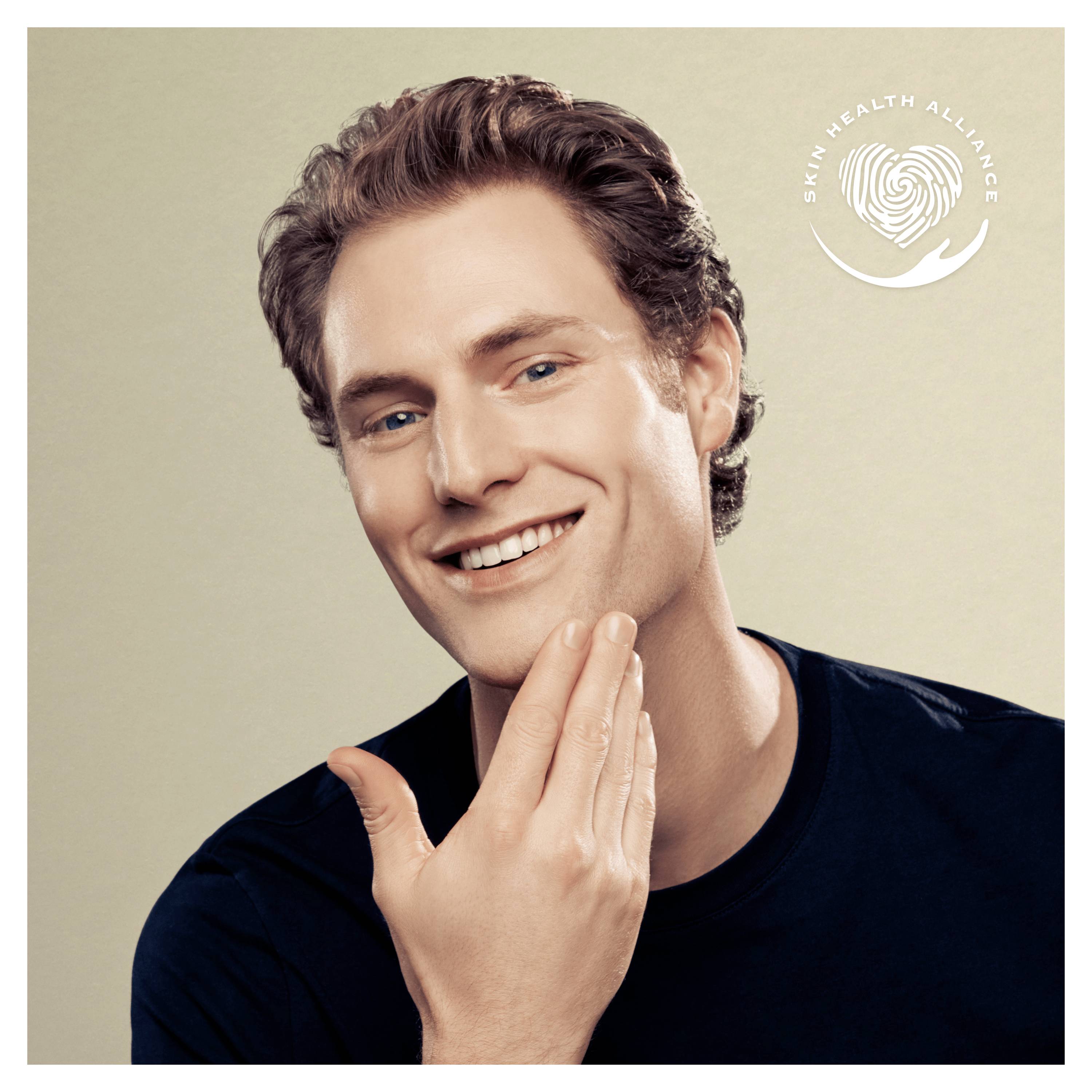 Een lachende man raakt zijn gezicht aan, met op de achtergrond het logo van de 'Skin Health Alliance'.