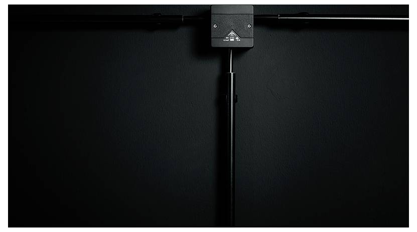 Een zwart metalen armatuur gemonteerd op een donkere muur, met horizontale en verticale stangen die zich uitstrekken vanuit een centrale doos.