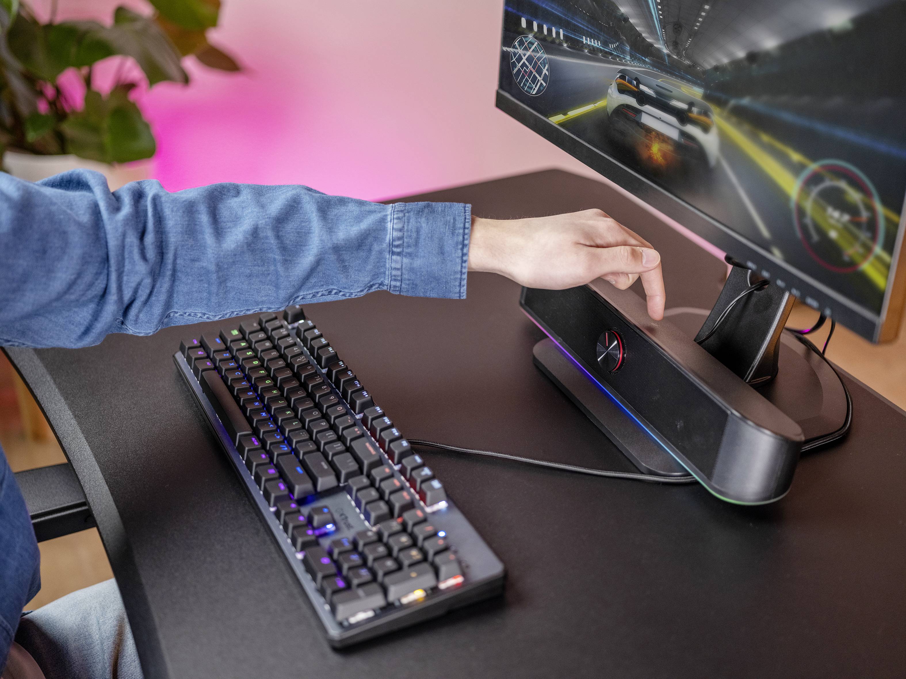 Een mens speelt een autoraces computerspel. Een hand rust op de luidspreker. Toetsenbord en monitor zijn zichtbaar.