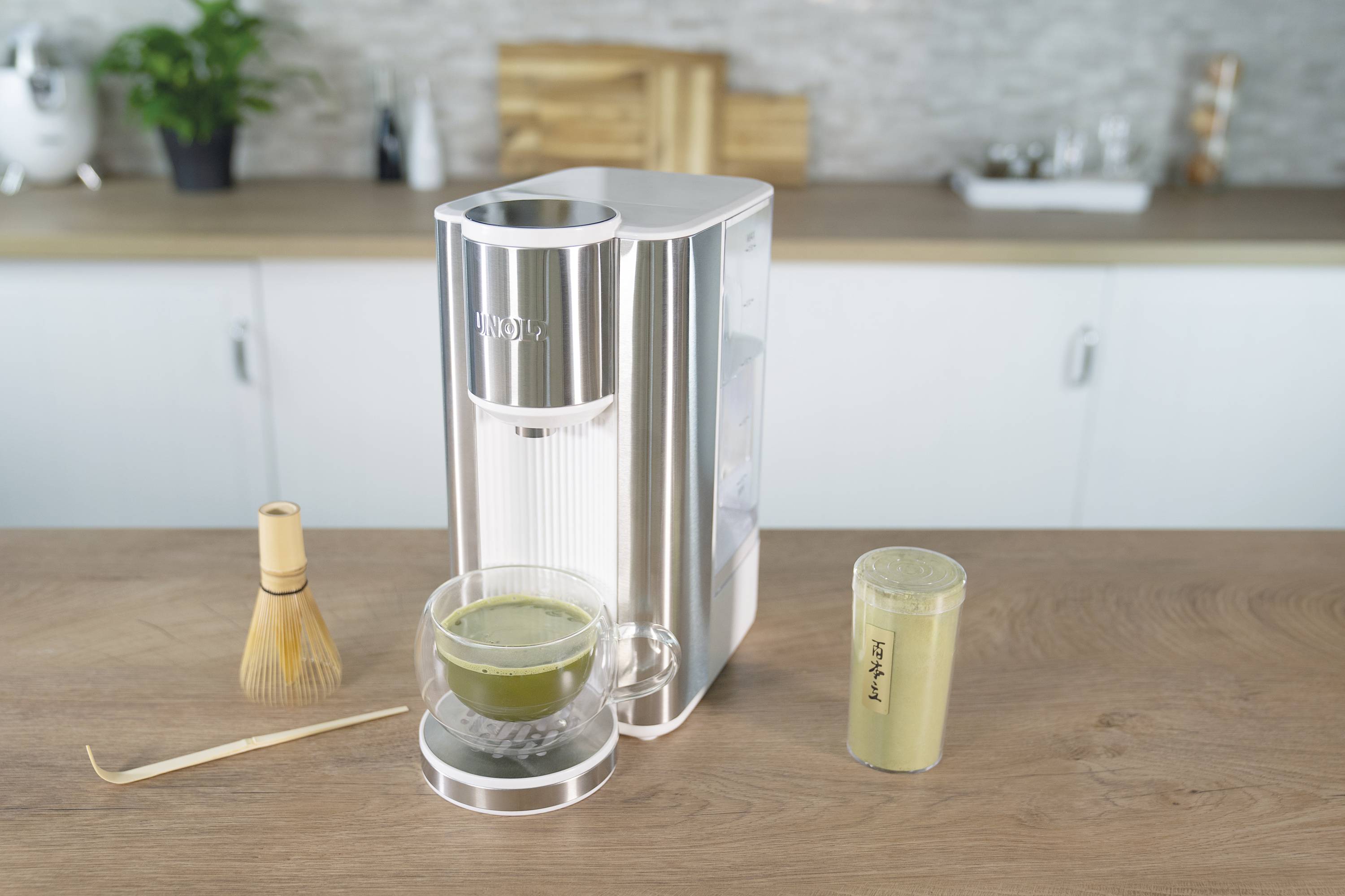 Een koffiemachine op een aanrecht, naast een kopje matcha en een bamboe klopper.