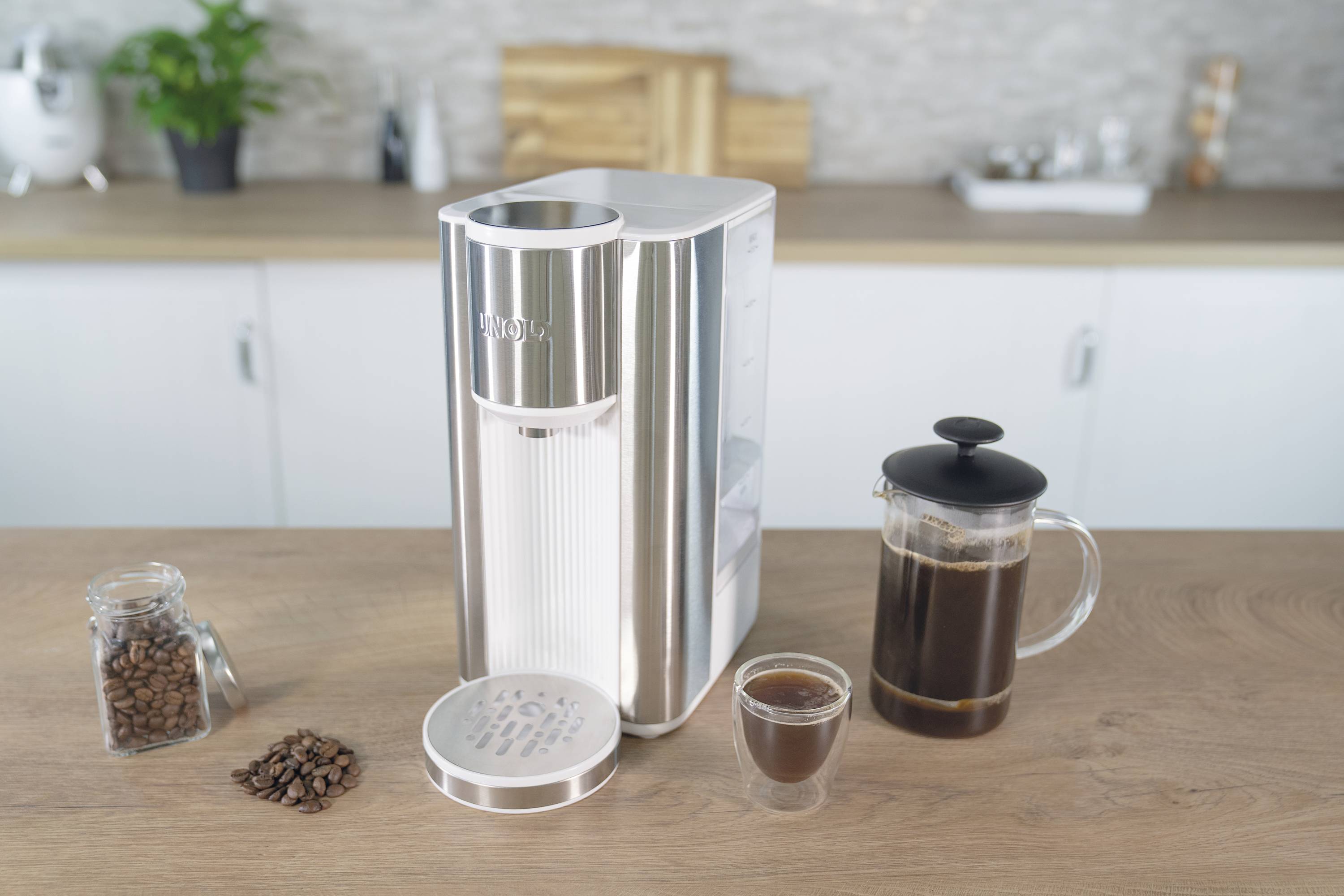 Koffiemachine op een aanrecht met een glazen kopje koffie, koffiebonen en een koffiepers ernaast.