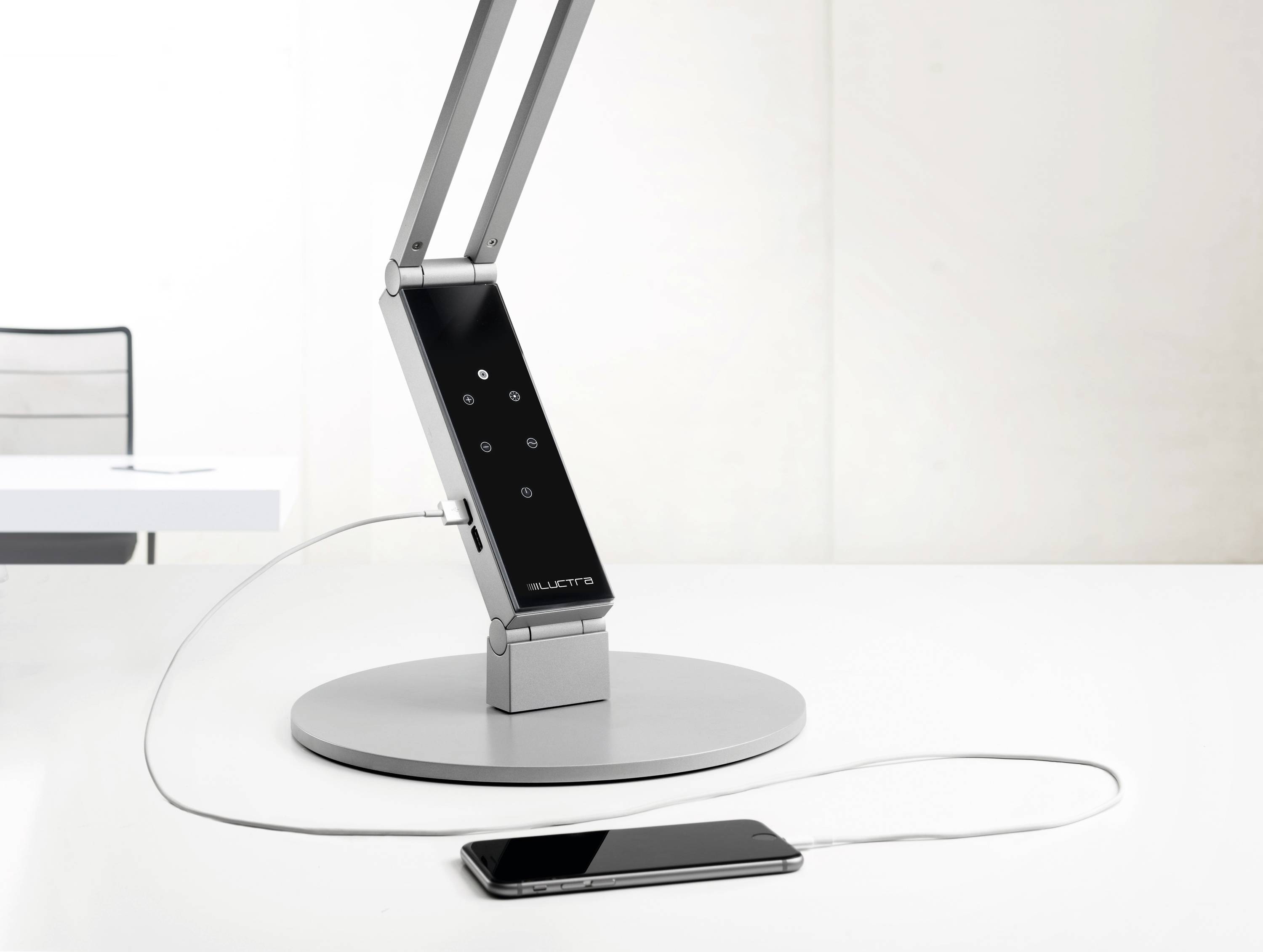 Een moderne bureaulamp met aanraakbedieningspaneel en USB-laadaansluiting laadt een smartphone op aan tafel.