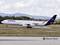 Een Lufthansa-vliegtuig, een Airbus A340, landt op een landingsbaan met rooksporen van de banden. Op de achtergrond zijn bergen zichtbaar.