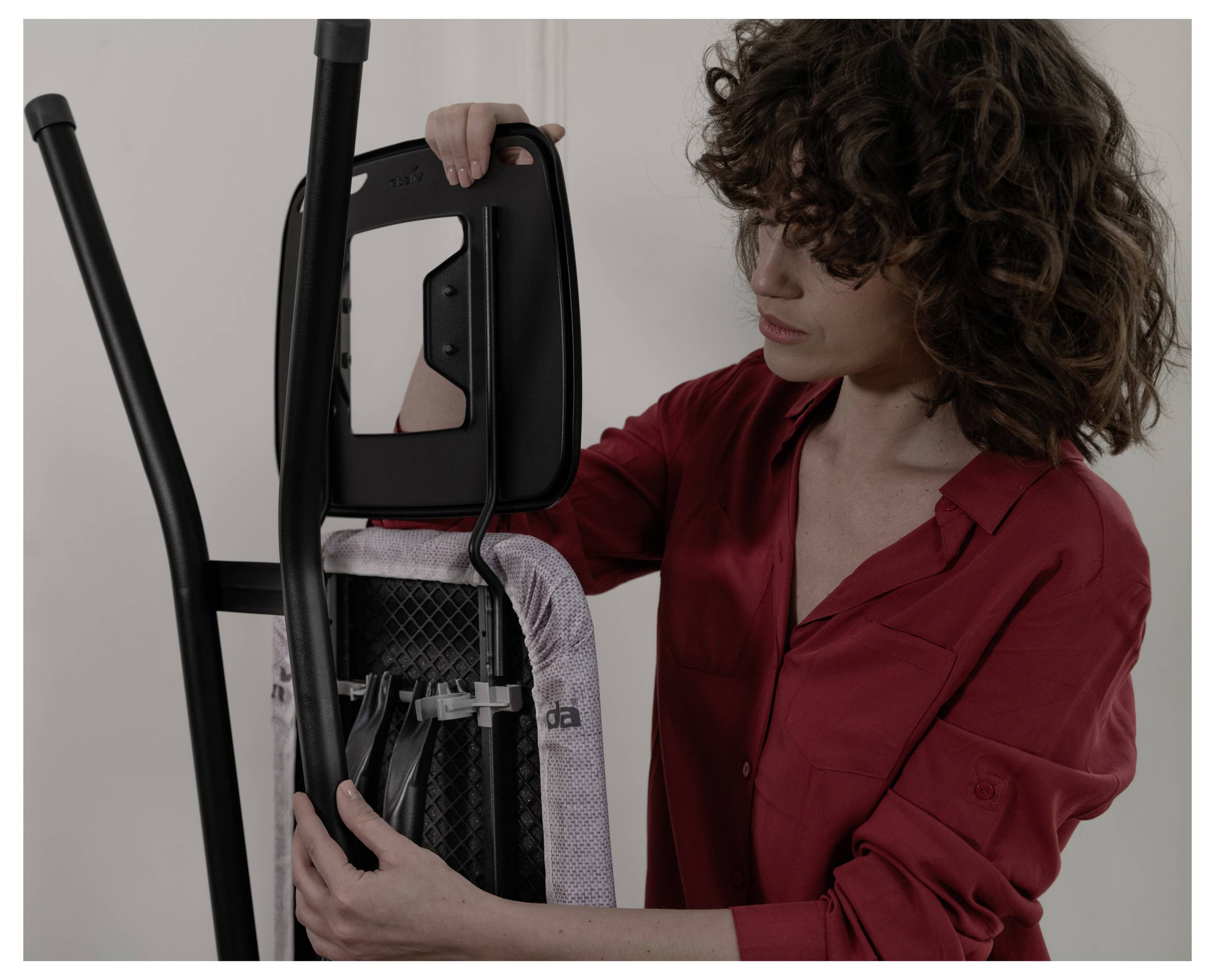 Vrouw in een rode blouse stelt en vouwt een trainingsapparaat tegen de muur.