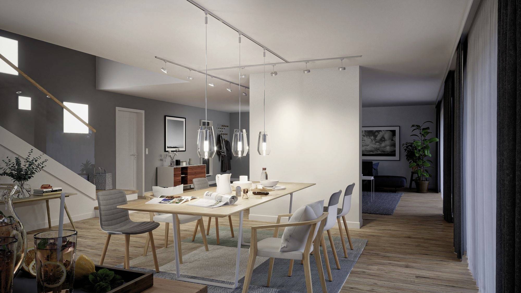 Een modern eetkamer met een lange houten tafel, omringd door zes stoelen. Een kroonluchter hangt boven de tafel. Op de achtergrond is een trap zichtbaar.