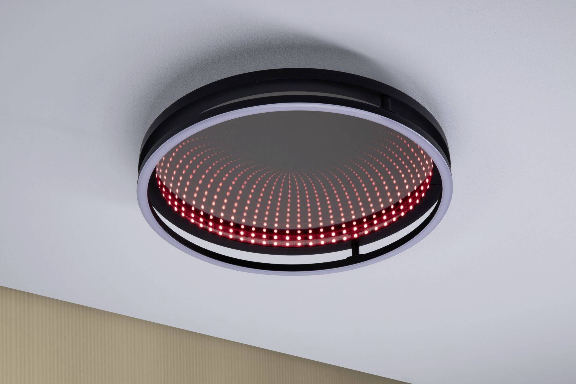 Ronde LED-plafondlamp met rood en wit lichtpatroon, modern ontworpen. Past bij een lichte ruimte met een beige wandsectie.