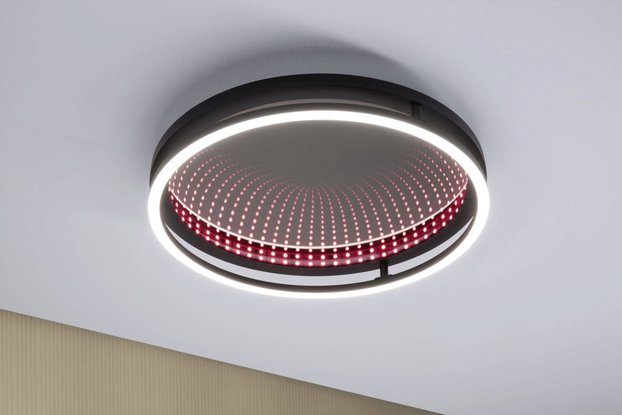Ronde plafondlamp met modern design: Een buitenste LED-ring verlicht wit, terwijl een binnenpatroon met rode verlichting een 3D-effect creëert.