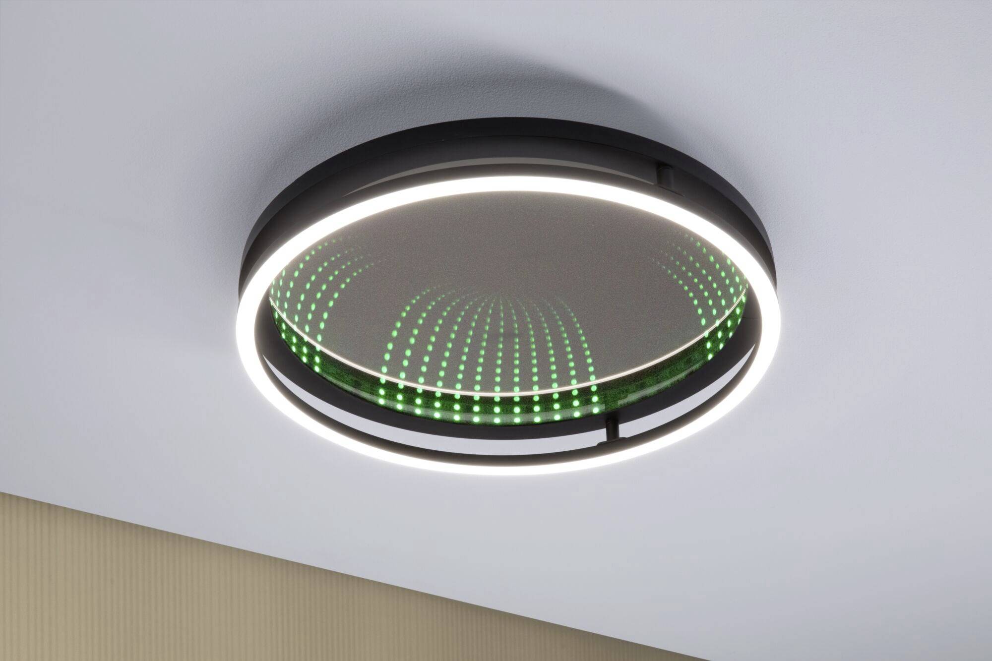 Een ronde plafondlamp met een zwart frame en een binnenste LED-lichtring. Het spiegelende oppervlak eronder toont groene LED-puntjes.