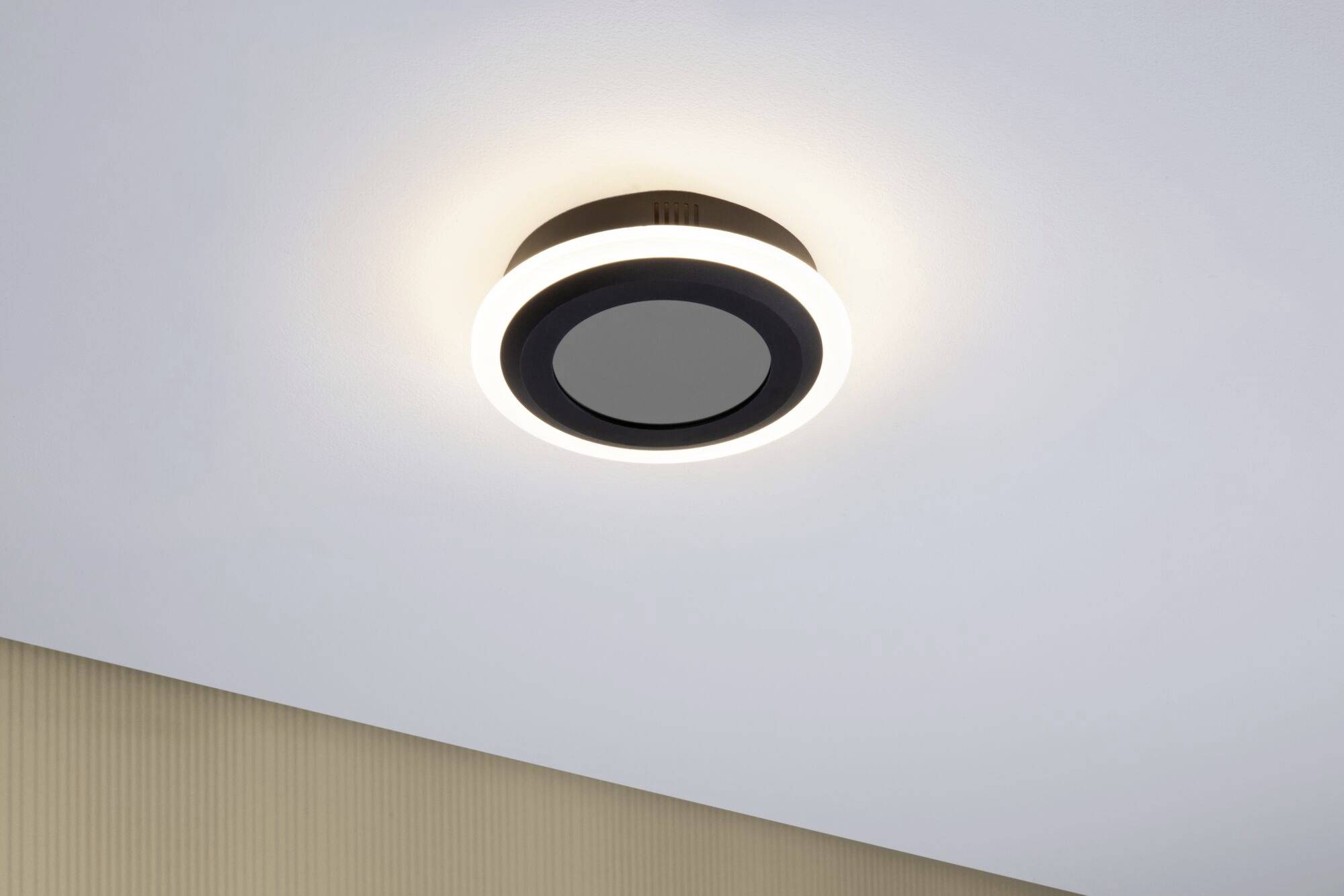 Plafondlamp in modern design met een cirkelvormige, lichtgevende rand aan een witte plafond, verspreidt warm licht.