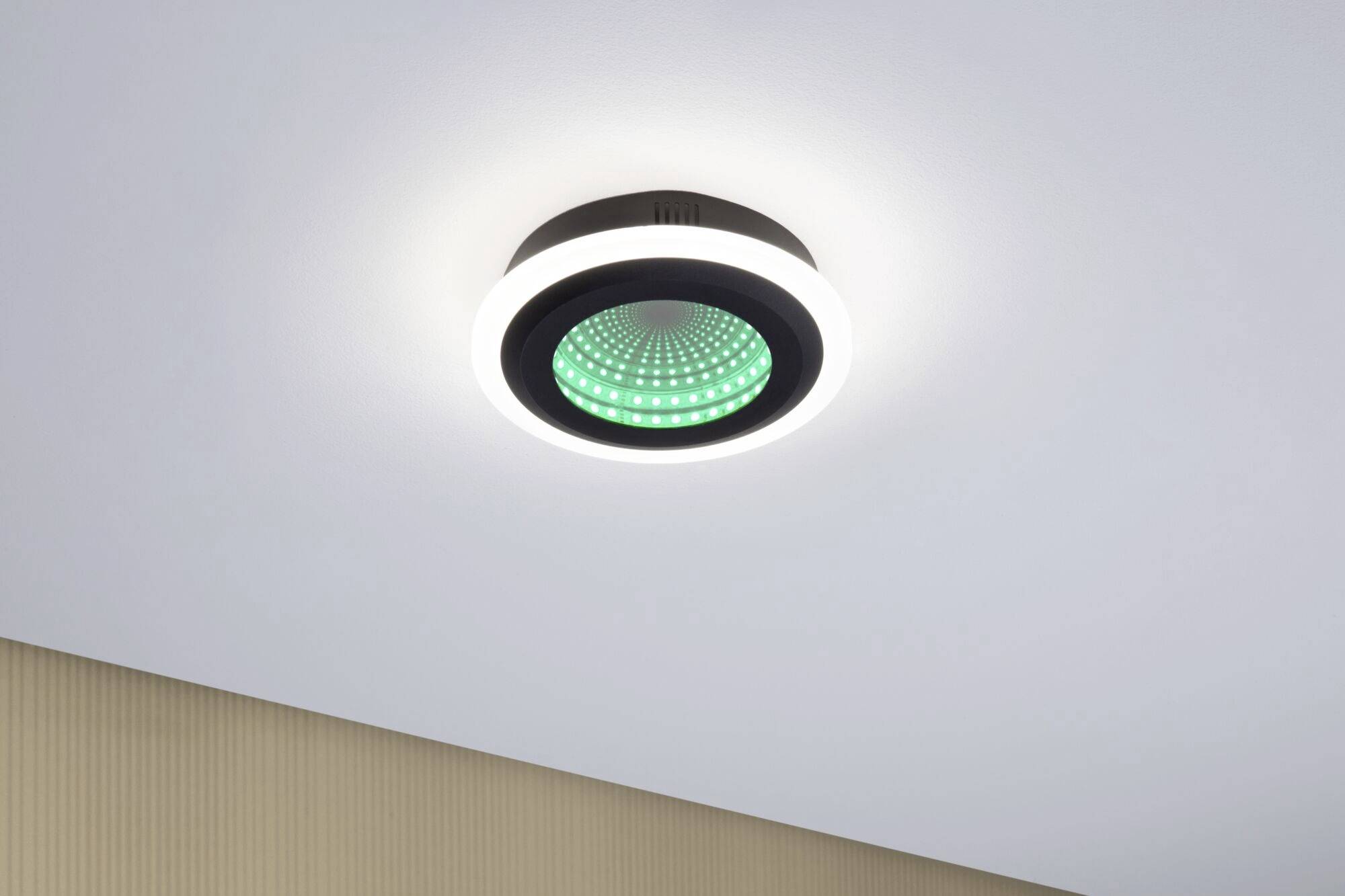 Een moderne, ronde plafondlamp met groen verlichte elementen aan de onderkant, gemonteerd aan een lichte plafond in een hedendaagse ruimte.