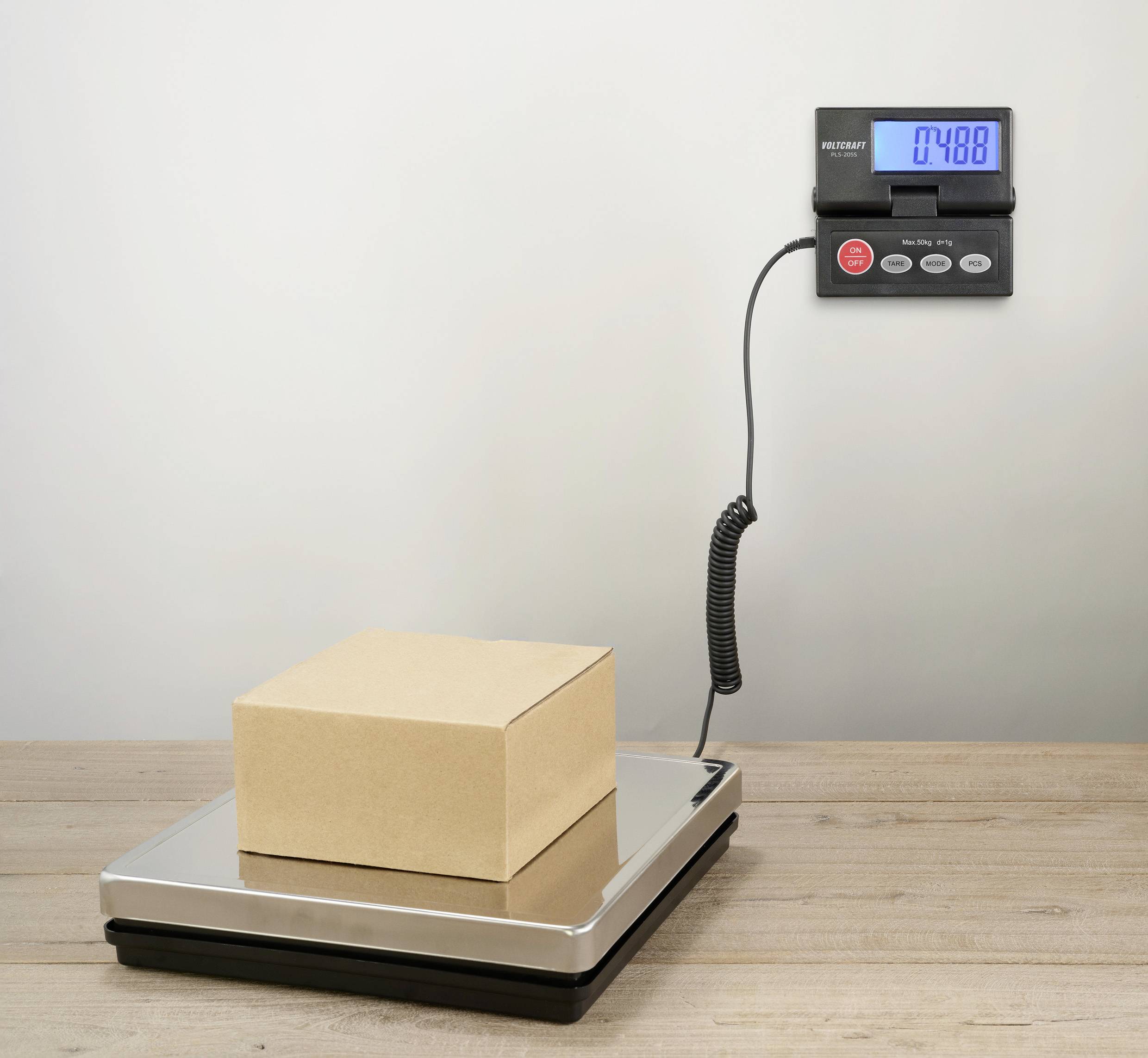 Een kartonnen doos staat op een digitale weegschaal die een gewicht van 7,488 kg aangeeft.