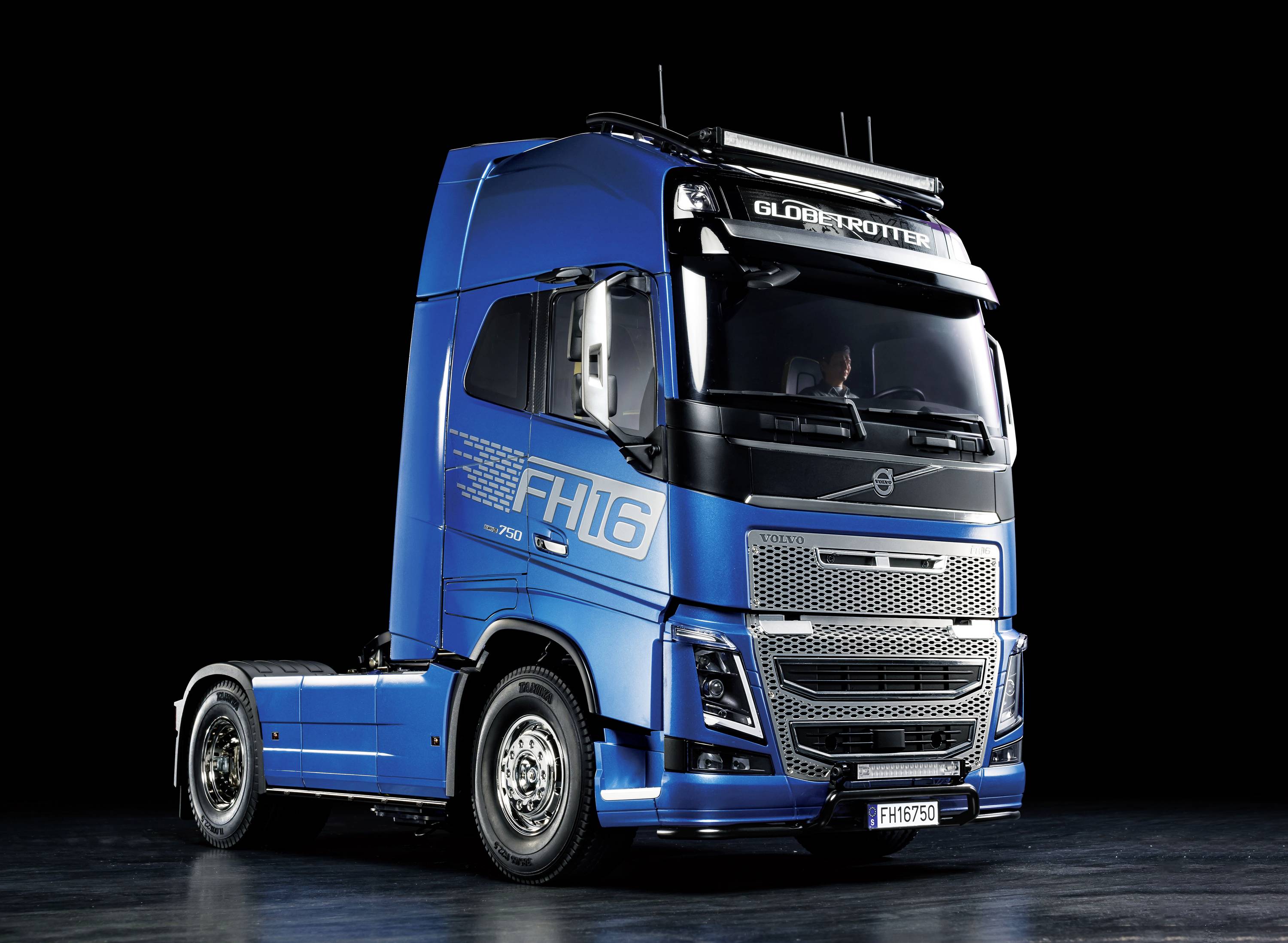 Een blauwe vrachtwagen met het opschrift 'FH16' staat op een zwarte achtergrond. Het betreft een modern, aerodynamisch model.