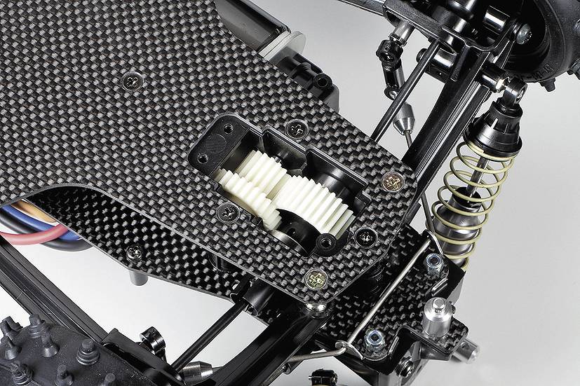 Close-up van een radiografische auto met gedetailleerde blik op de koolstofvezel chassisplaat en tandwielconstructie.